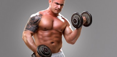 Bodybuilder with a tattoo lifting dumbells, closeup